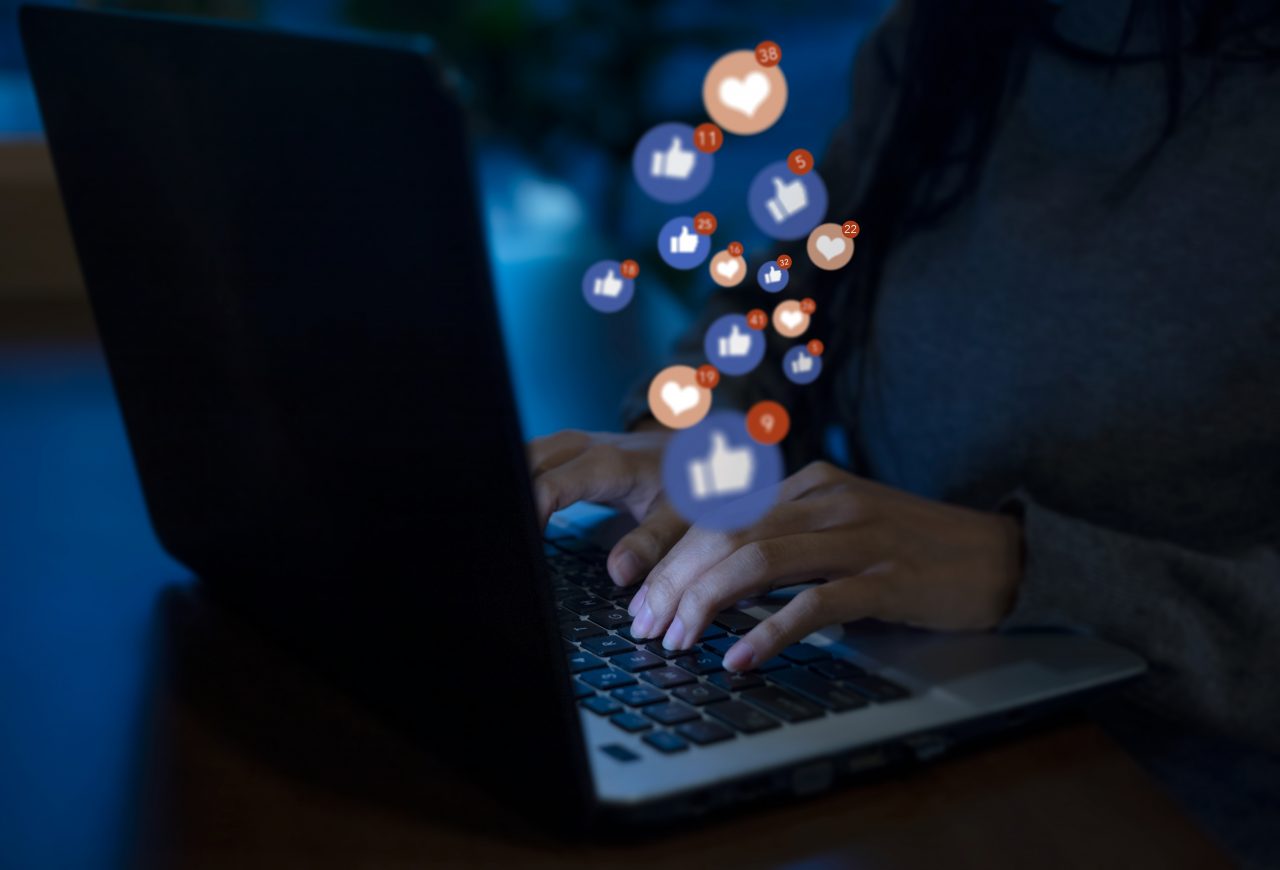 Person browses Facebook with social icons floating above keyboard